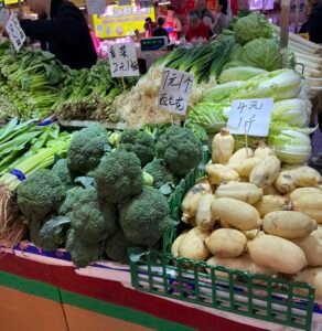 Shengfu Xiaoguan Market: Between Tradition, Everyday Life, and Change Fresh vegetables including broccoli, cabbage, and lotus roots with handwritten price tags at Shengfu Xiaoguan Market in Beijing.