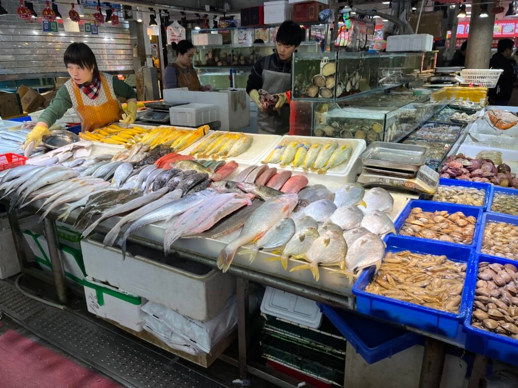 Shengfu Xiaoguan Market: Between Tradition, Everyday Life, and Change A vendor organizing fresh seafood, fish, and clams on ice at a bustling Chinese fresh market in Beijing.