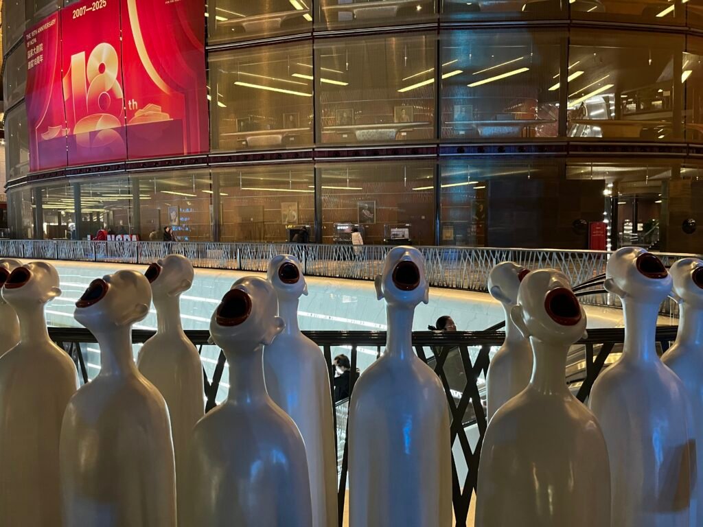 A contemporary art installation featuring rows of white statues with open mouths singing, displayed inside the NCPA Beijing.