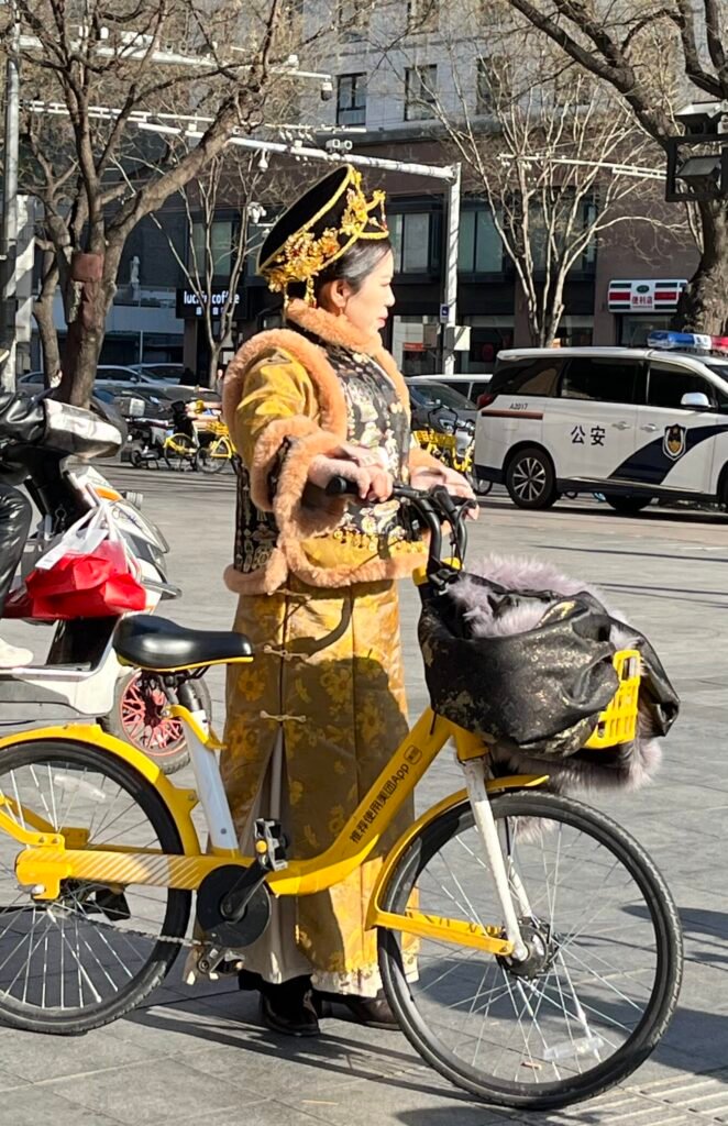 Hanfu in China: When Traditional Dress Moves through Modern Life Chinese woman in golden winter Hanfu riding a modern yellow shared bicycle on a city street.